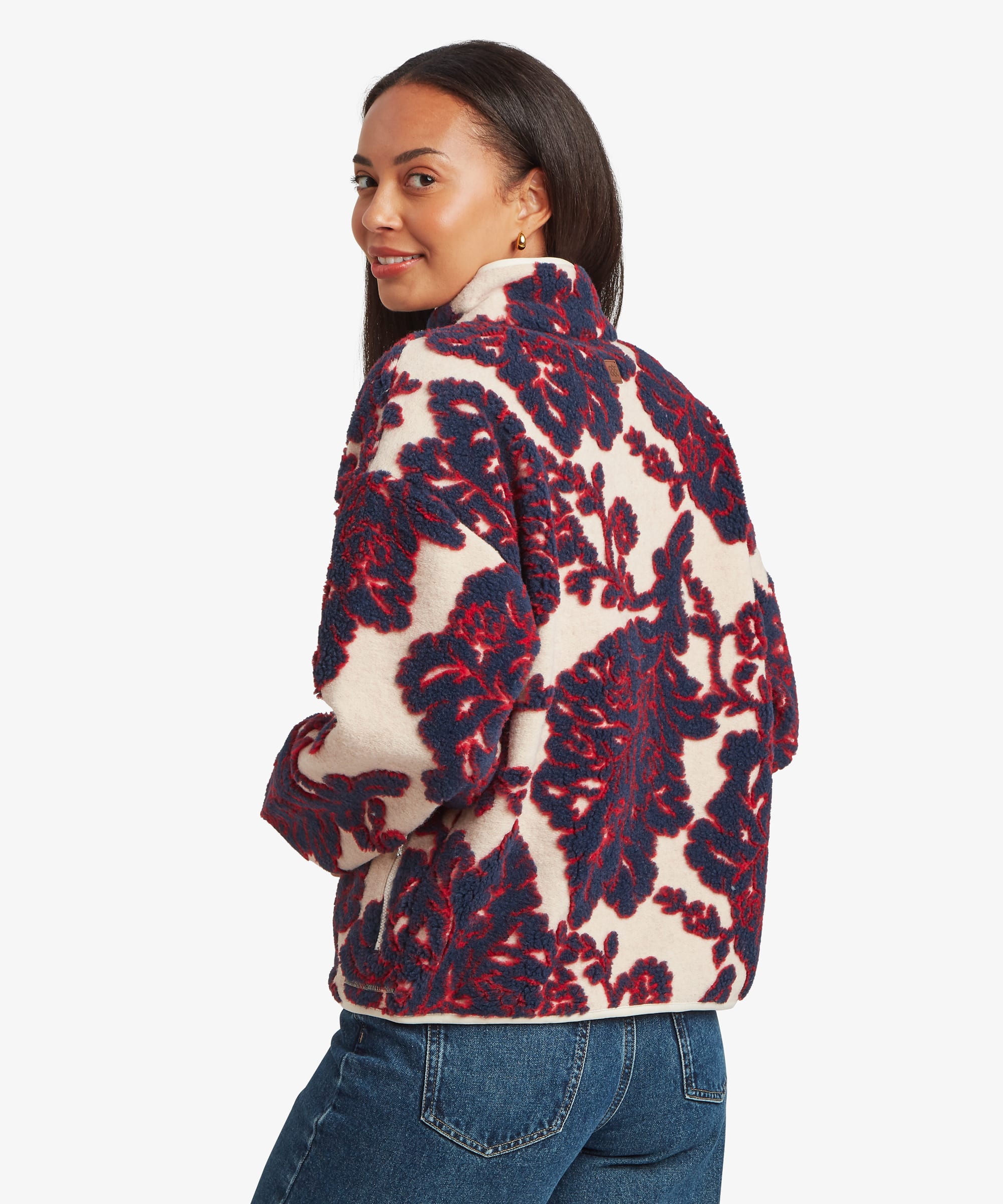 Rear studio view of a woman wearing a cream fleece jacket with a bold burgundy floral print extending across the back and sleeves. The image highlights the pattern placement and relaxed fit.