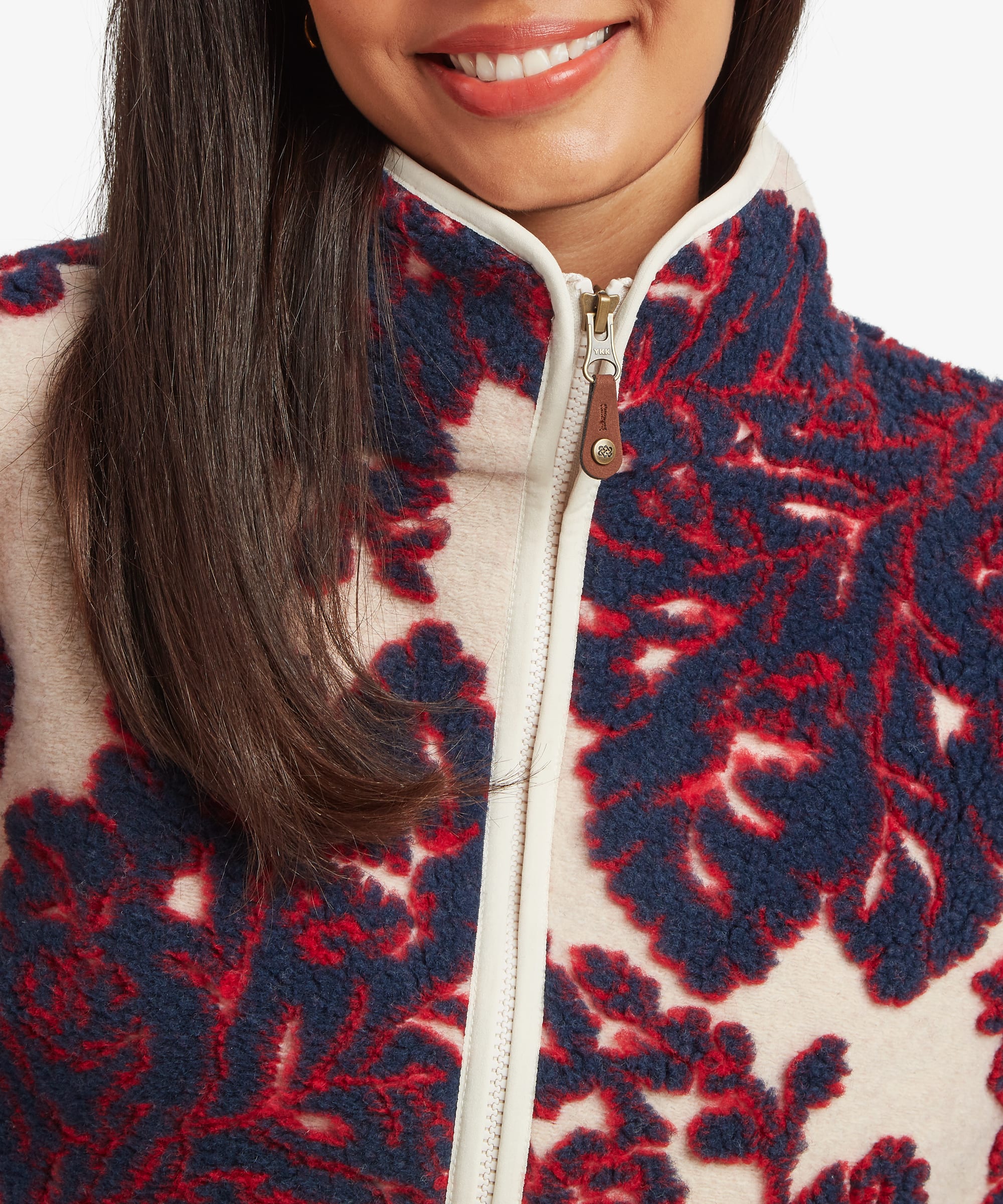 Close-up portrait of a woman wearing a cream fleece jacket with a burgundy floral design. The image focuses on the stand collar, full zip closure, and detailed botanical pattern around the chest and neckline.
