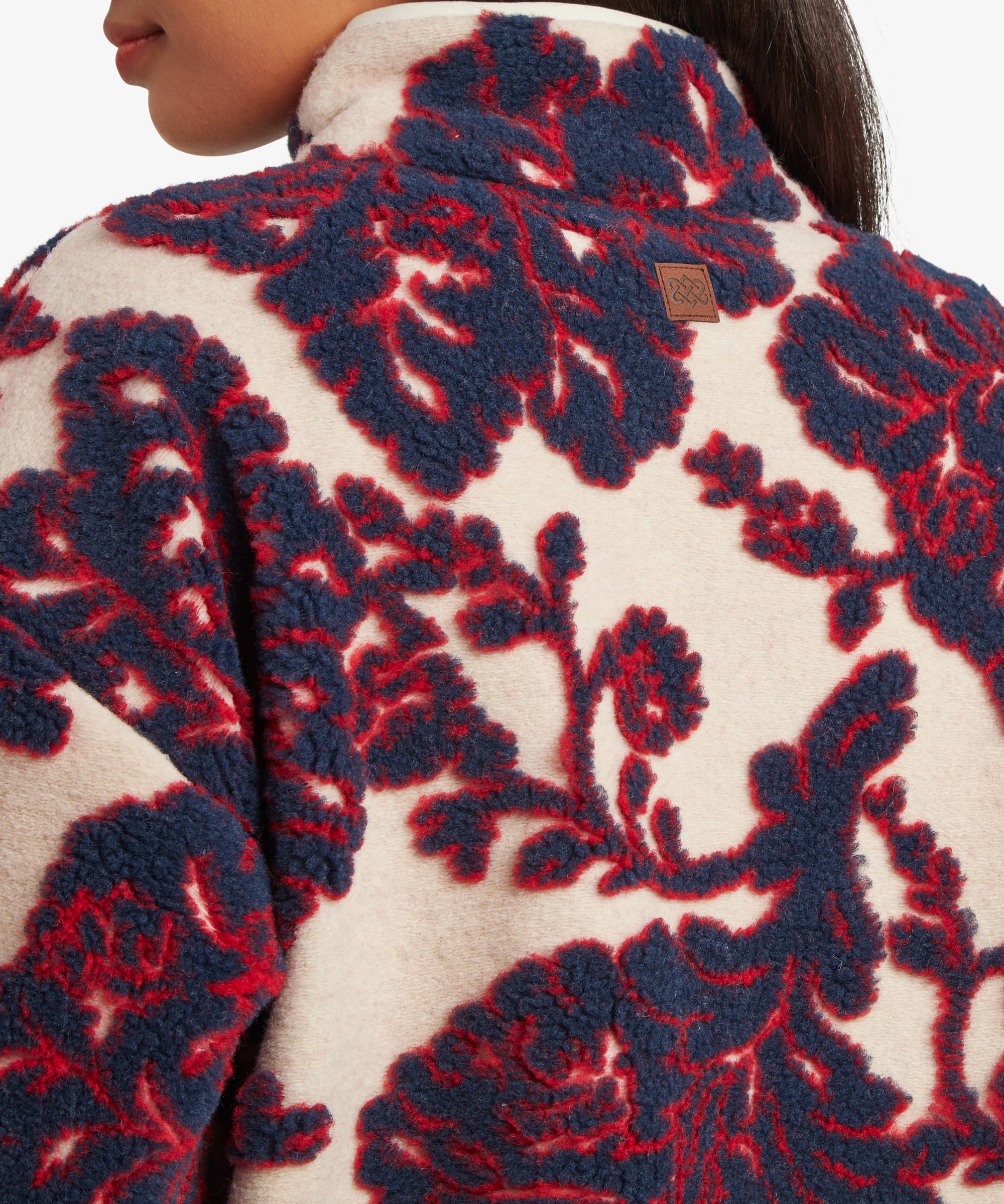 Close-up detail of the cream floral fleece jacket showing the high collar, zipper construction, and oversized burgundy botanical print across the upper body.