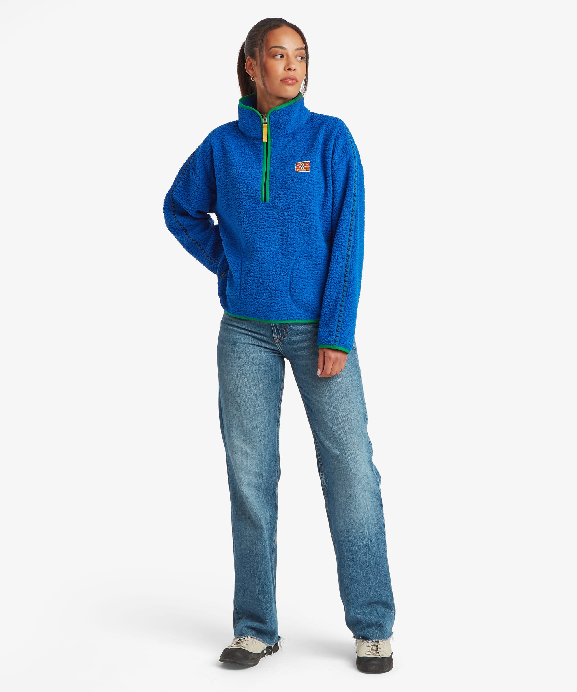 Full-length studio image of a woman wearing a bright blue quarter-zip fleece pullover with a high stand collar and contrasting green zip detail. Styled with blue jeans, the image highlights the pullover's relaxed silhouette.