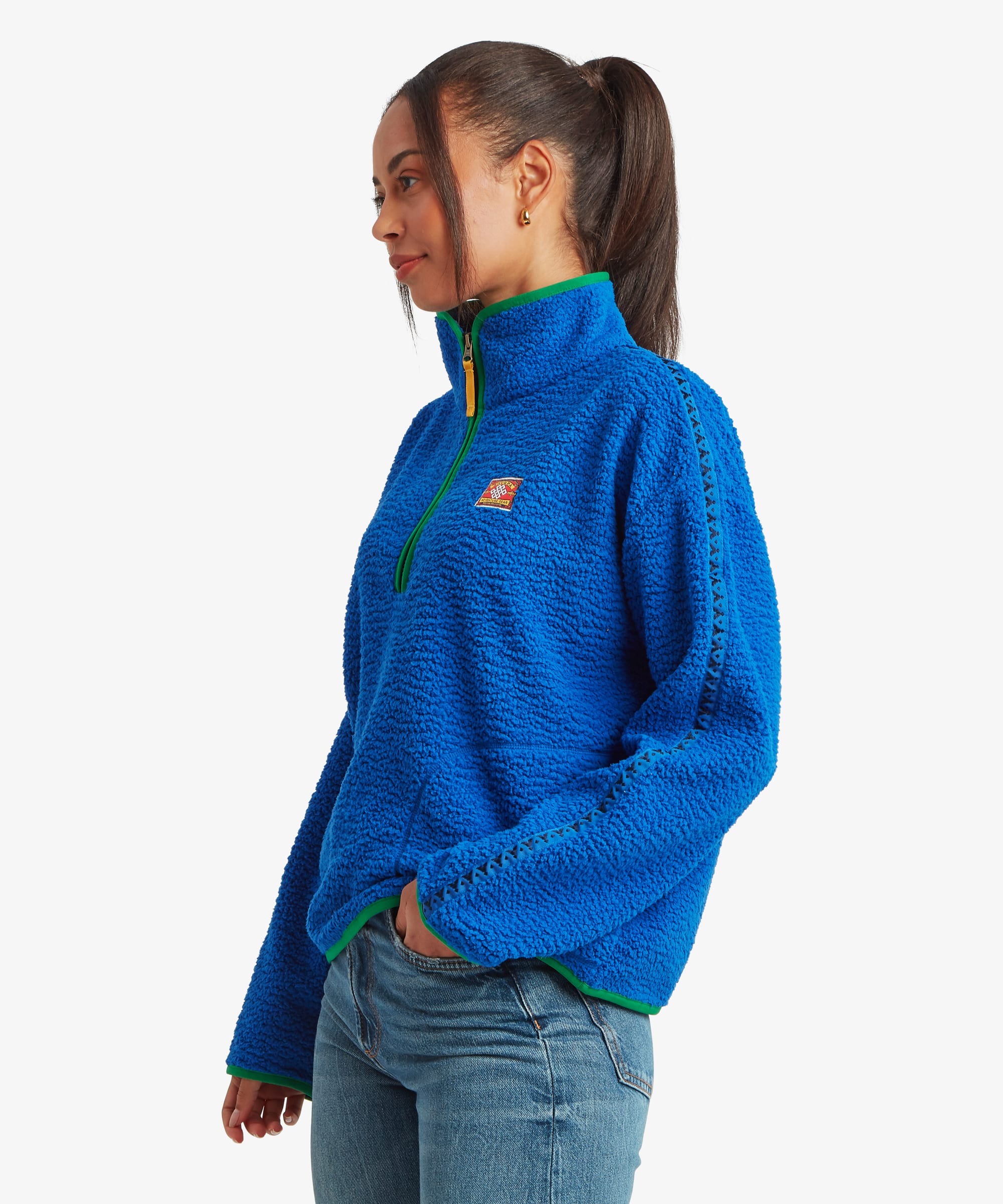 Side-profile studio view of a woman wearing a bright blue fleece pullover with a quarter-zip neckline and contrasting trim accents. The image showcases the shape and drape of the garment from the side.