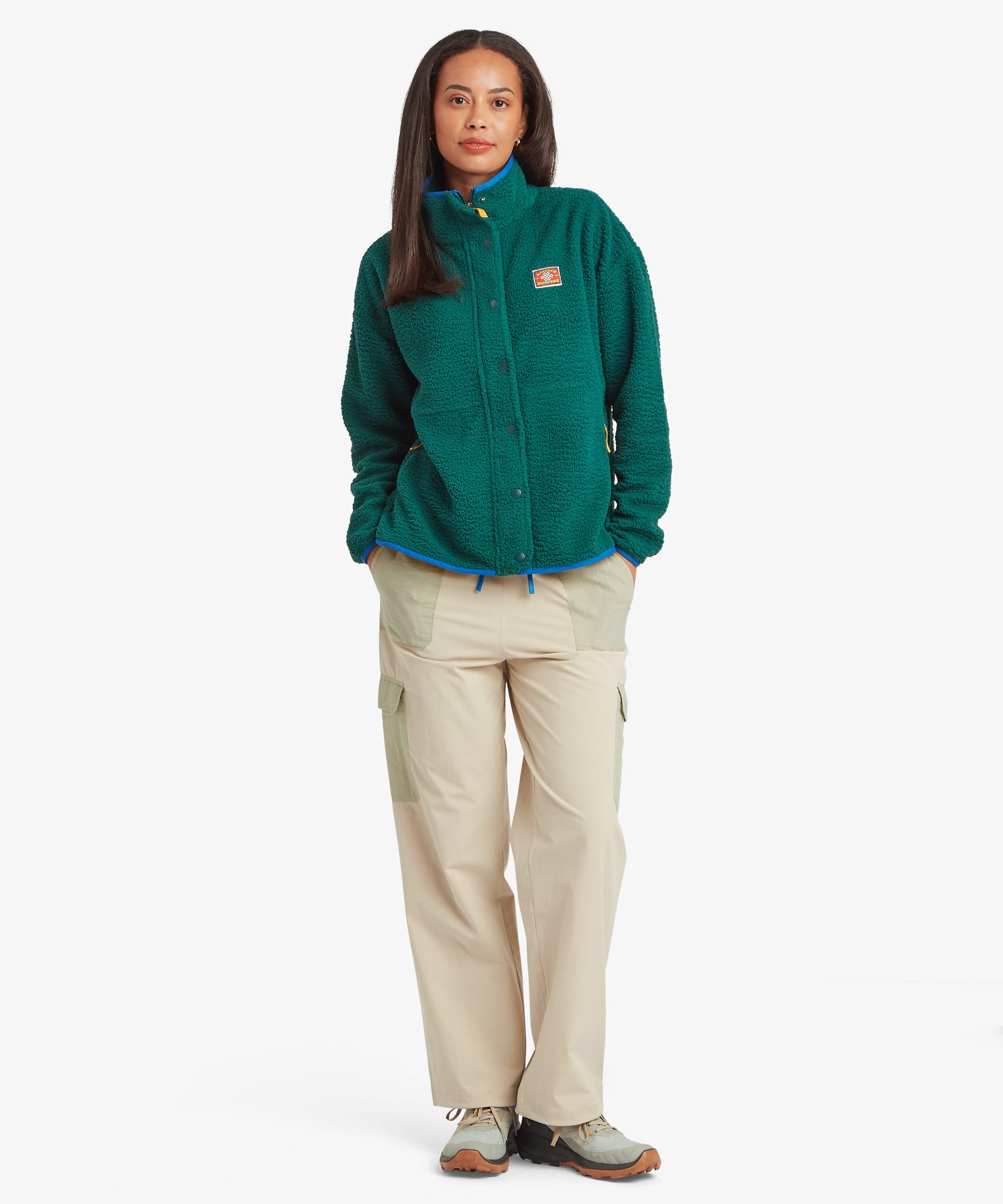 Full length view of a woman wearing a green fleece jacket and beige pants on a white background