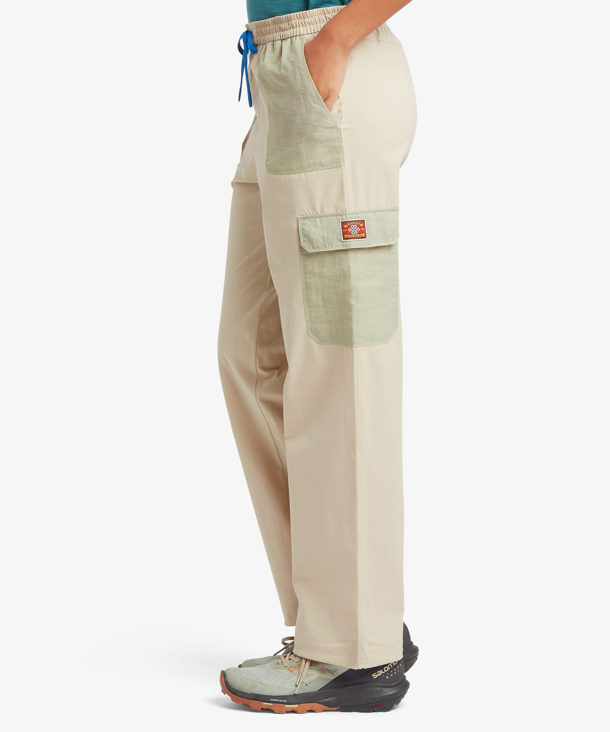 Side view of a woman wearing beige and green cargo pants with a visible brand logo on a white background