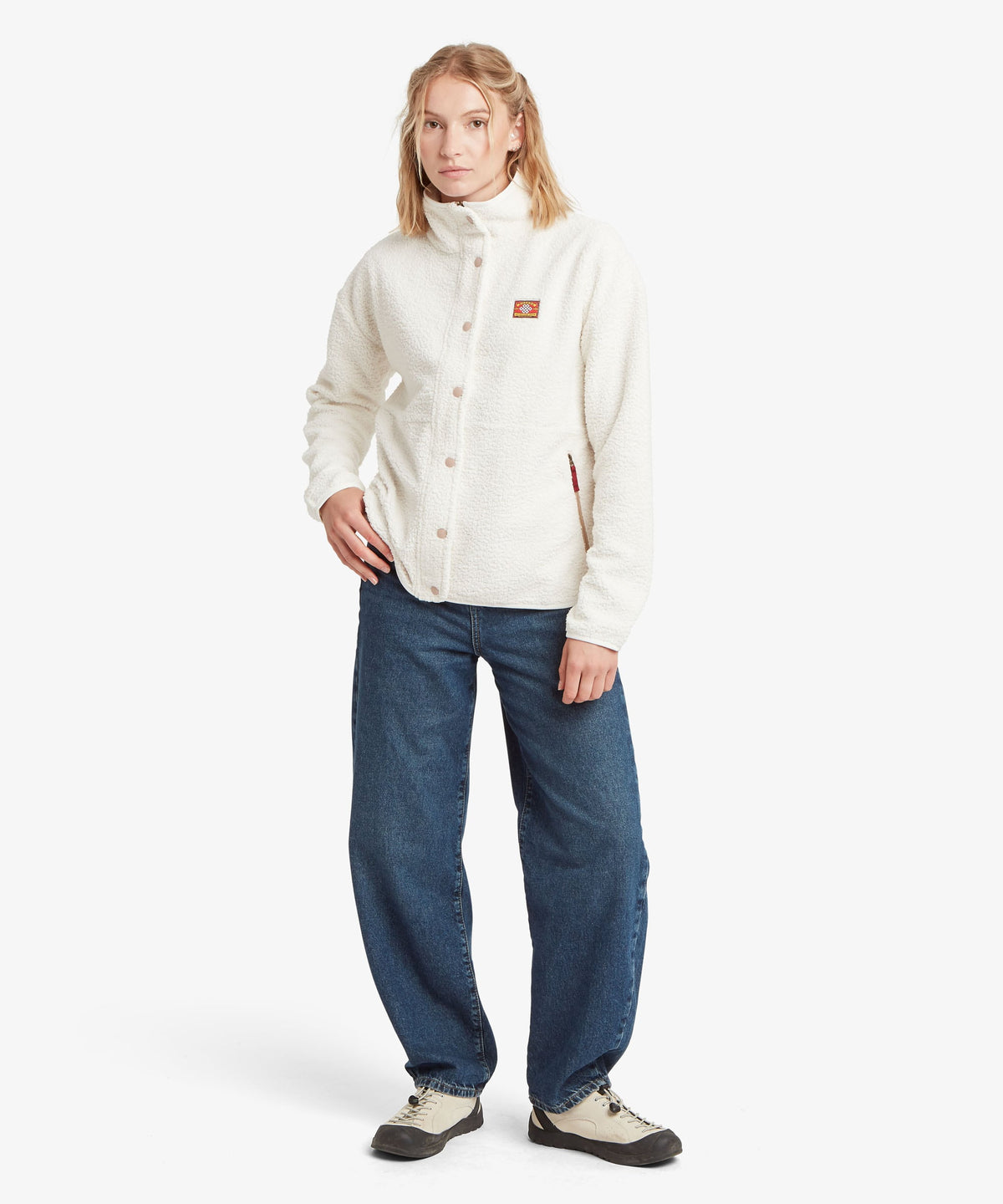 A female model in the white Tarcho Full-Zip Jacket by Sherpa Adventure Gear with a high collar.
