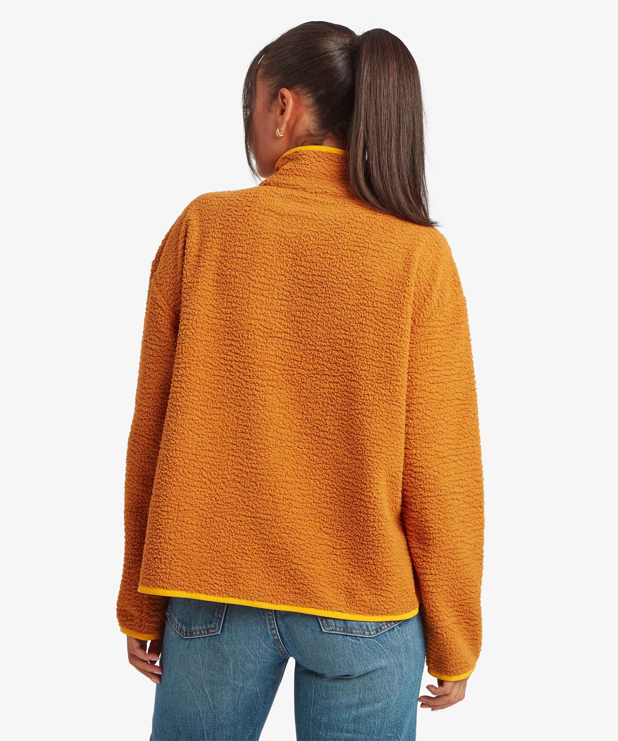 Rear studio view of a woman wearing a mustard-yellow fleece jacket paired with blue jeans. The image highlights the clean back design, relaxed fit, and slightly curved hemline.