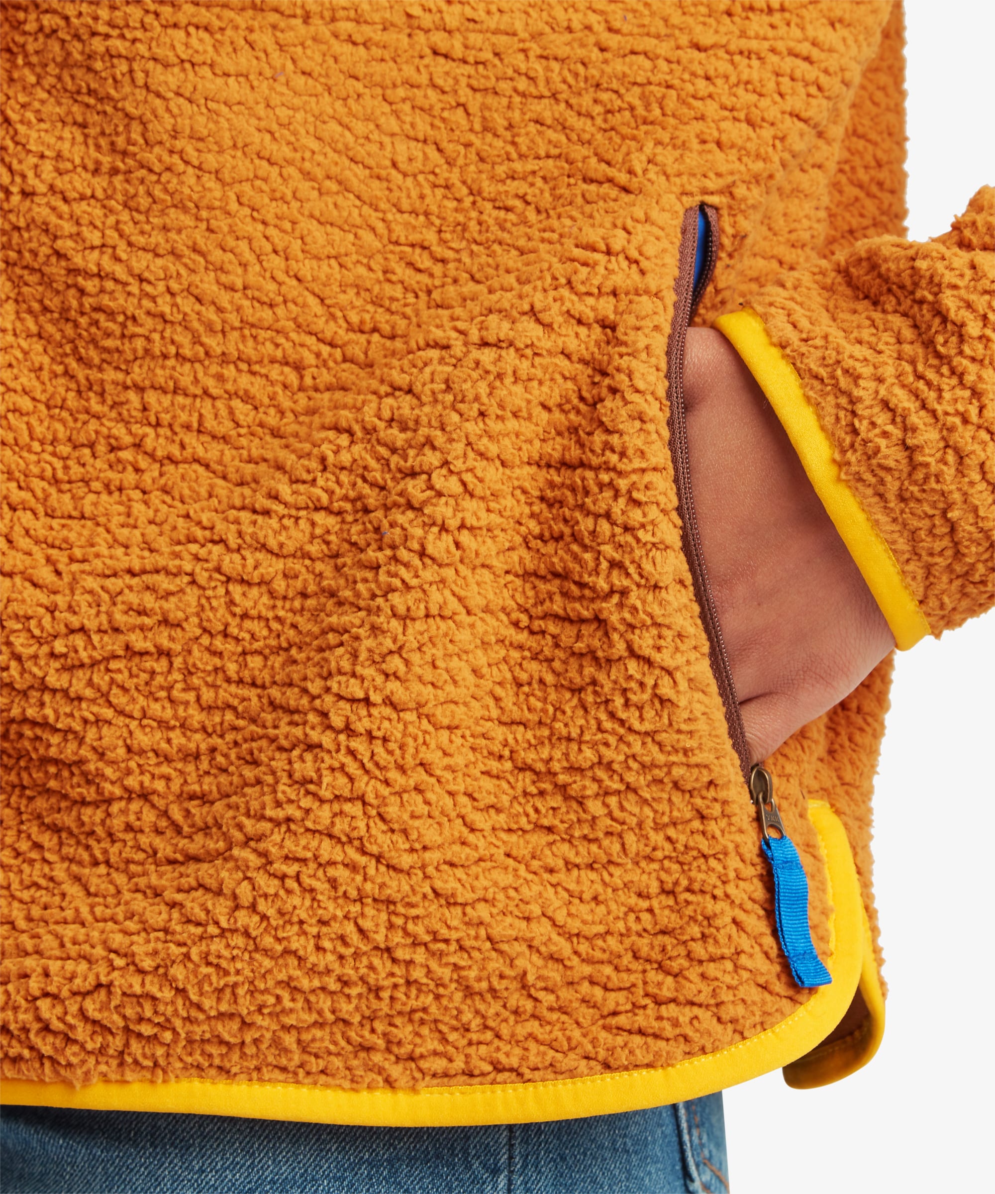 Detailed close-up of the mustard-yellow fleece jacket showing the textured fleece surface, zippered pocket opening, and contrasting trim details along the hem and pocket edge.