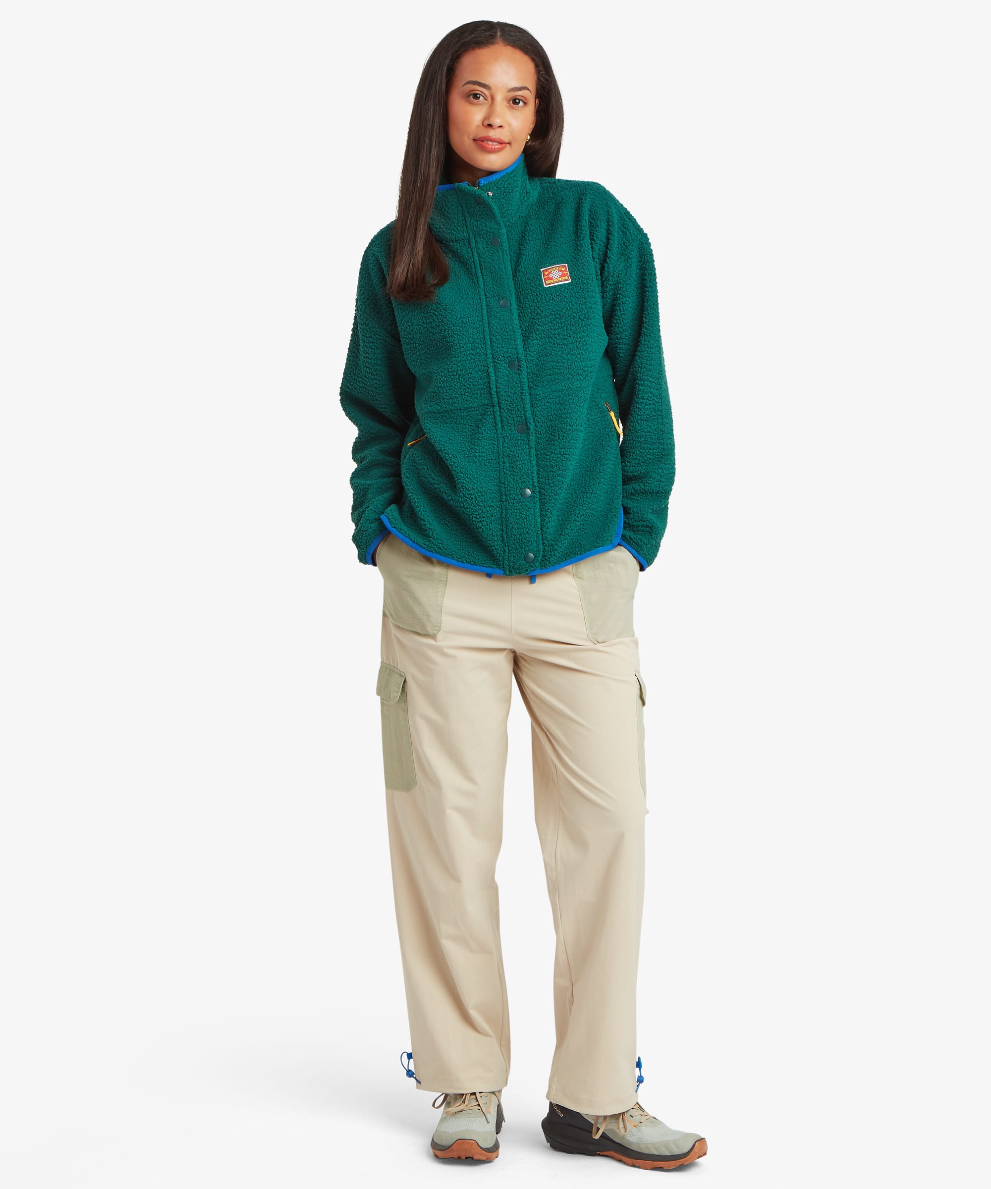 Full-length studio image of a woman wearing a deep green fleece jacket with a full front zip and stand collar. Styled with beige trousers, the image showcases the overall shape and proportions of the garment.