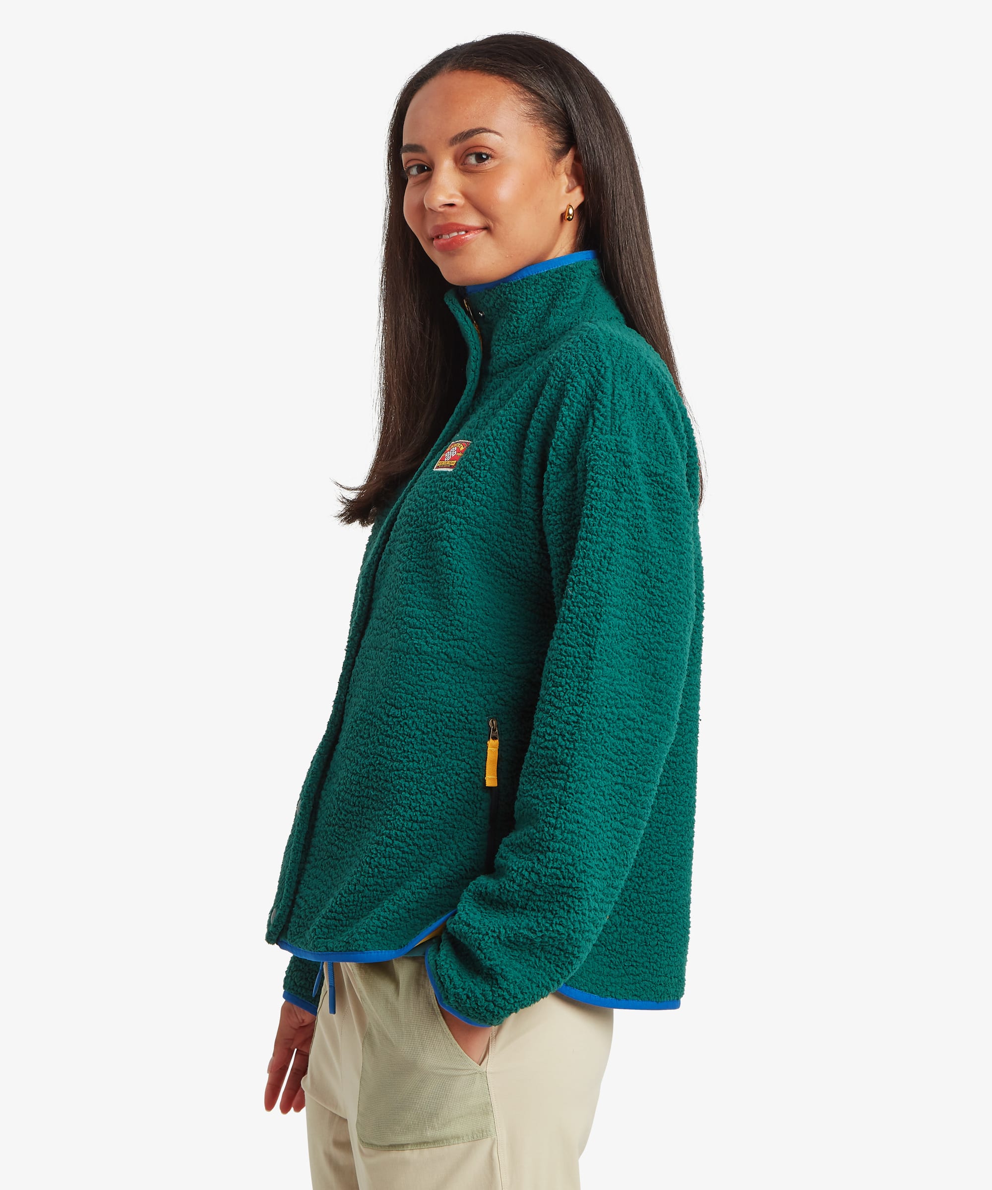 Side-profile studio view of a woman wearing a deep green fleece jacket with a relaxed fit and high collar. The image highlights the jacket's drape and side profile.