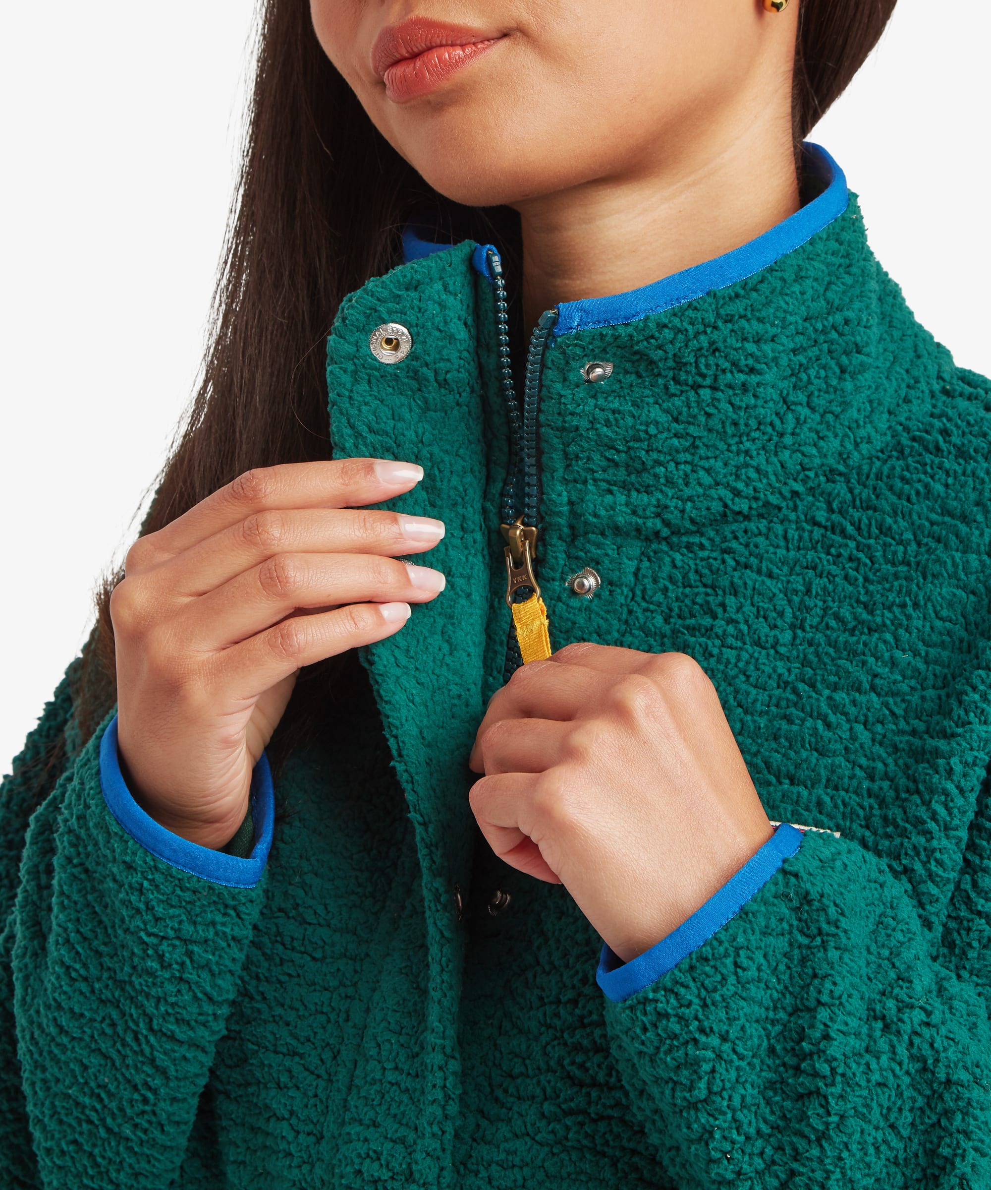 Close-up detail of a model holding the collar of a deep green fleece jacket. The image highlights the high neckline, zip closure, chest logo patch, and contrasting trim accents.