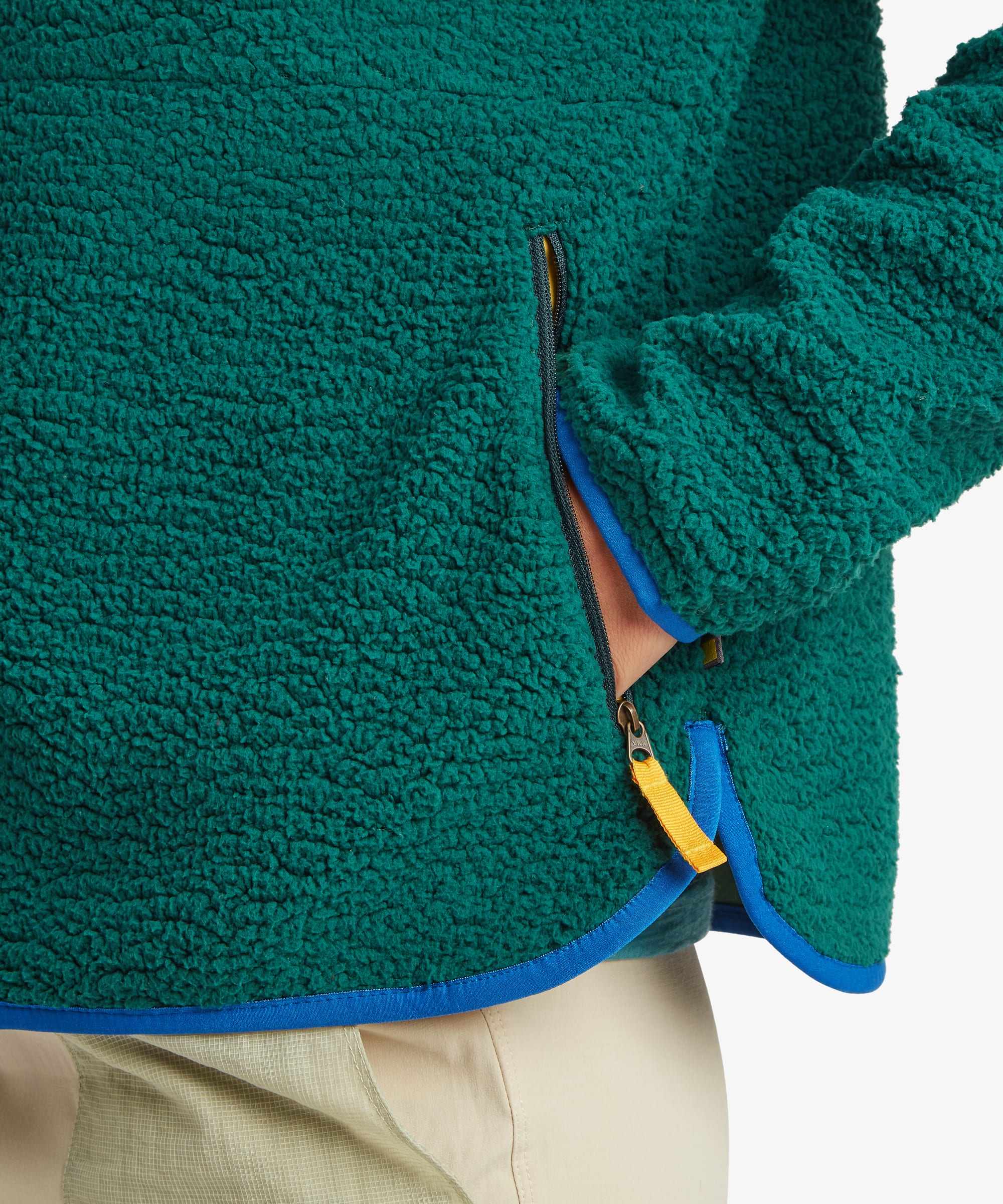 Close-up of the deep green fleece jacket showing the textured fleece fabric, zippered pocket detail, and contrasting trim at the hem and pocket opening.