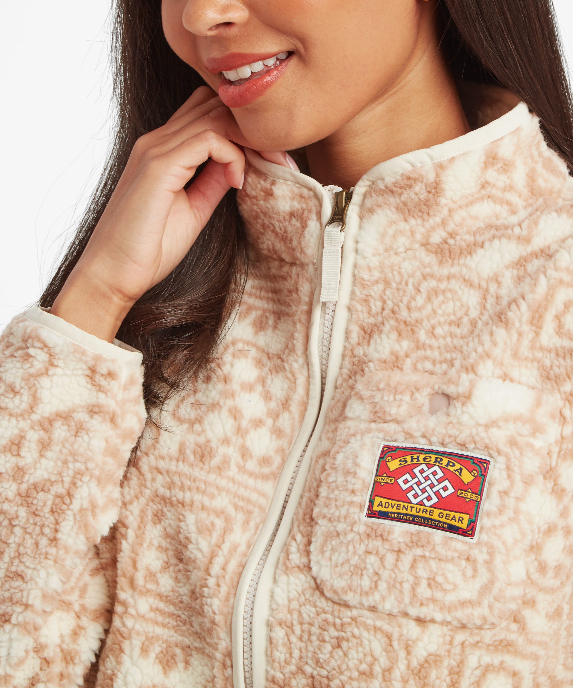 Close-up portrait of a woman wearing a cream fleece jacket with a tonal geometric print and full-length zip. The image highlights the stand collar, chest patch detail, and soft textured fabric.
