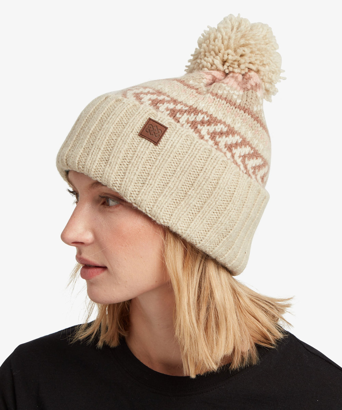 A woman in profile wearing a cream-colored knit beanie with a brown.