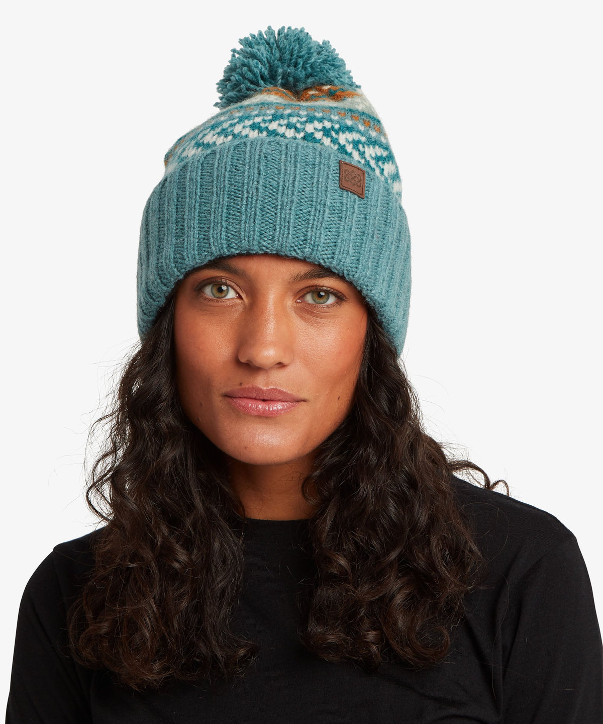 A woman wearing a teal blue knit pom-pom beanie with a white and blue patterned band.