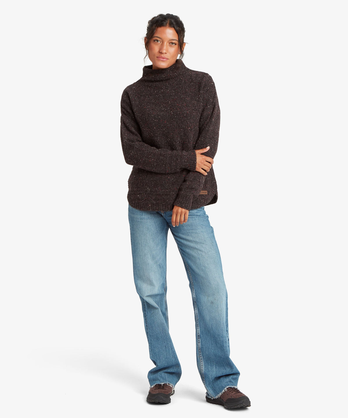 A female model wearing the black Yuden Sweater by Sherpa Adventure Gear with a high neckline.