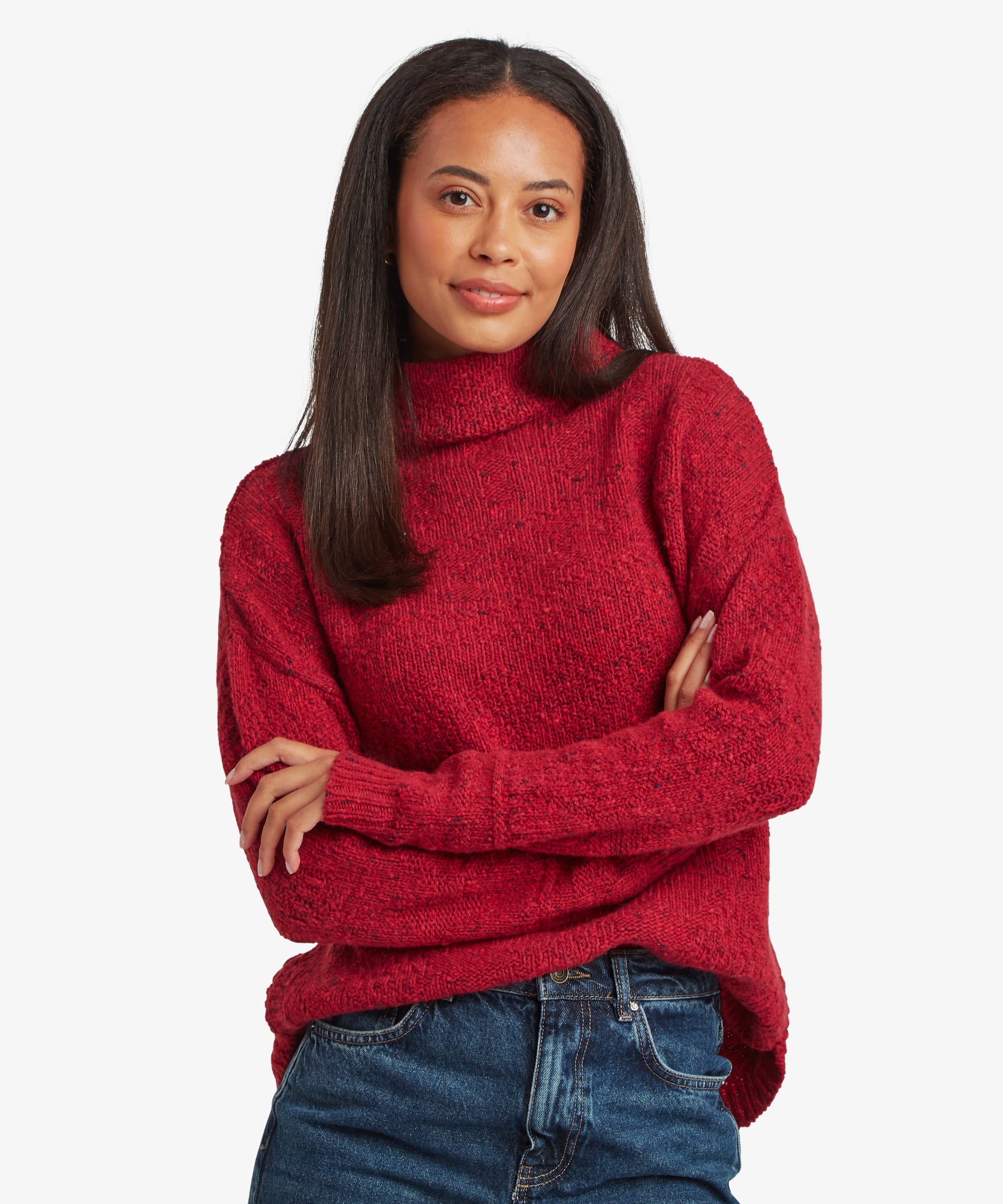 Woman standing against a plain studio background wearing a rich red knit sweater with a high mock-neck collar. She faces forward with her arms crossed, paired with blue jeans, creating a relaxed and confident look.