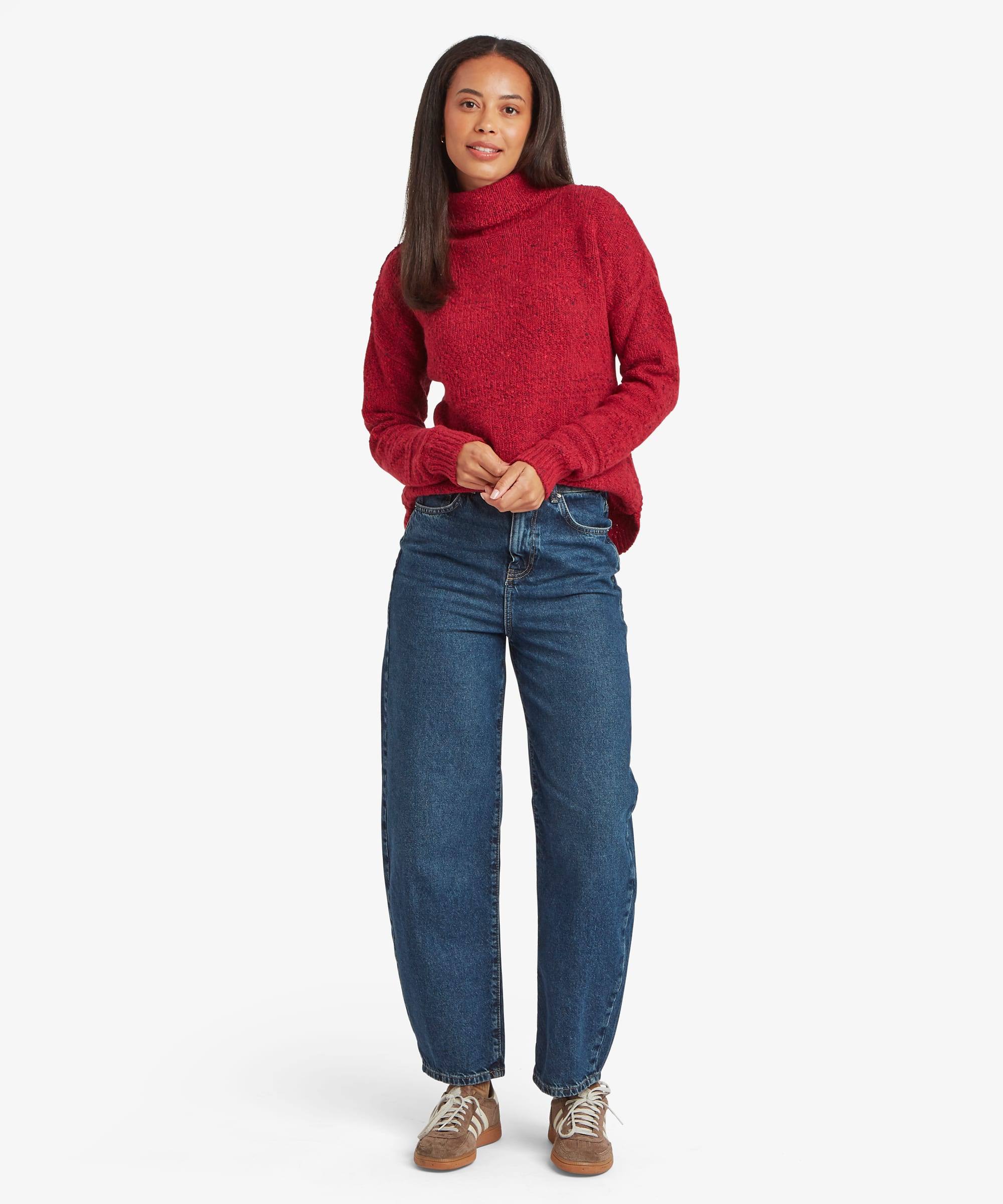 Full-length studio image of a woman wearing a red knit sweater with a high neckline and relaxed fit. Styled with blue jeans, the image highlights the sweater's overall silhouette and length.