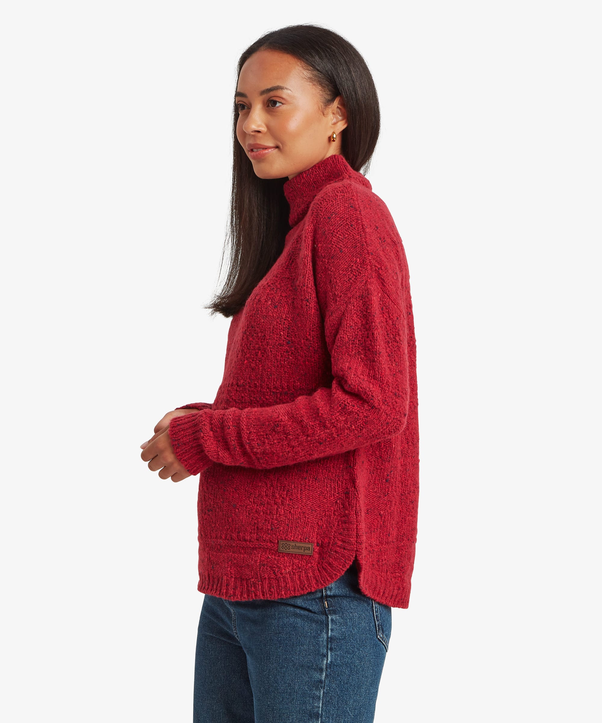Side-profile studio view of a woman wearing a red knit sweater with a softly structured high collar and relaxed fit. The image showcases the sweater's shape through the body and sleeves.
