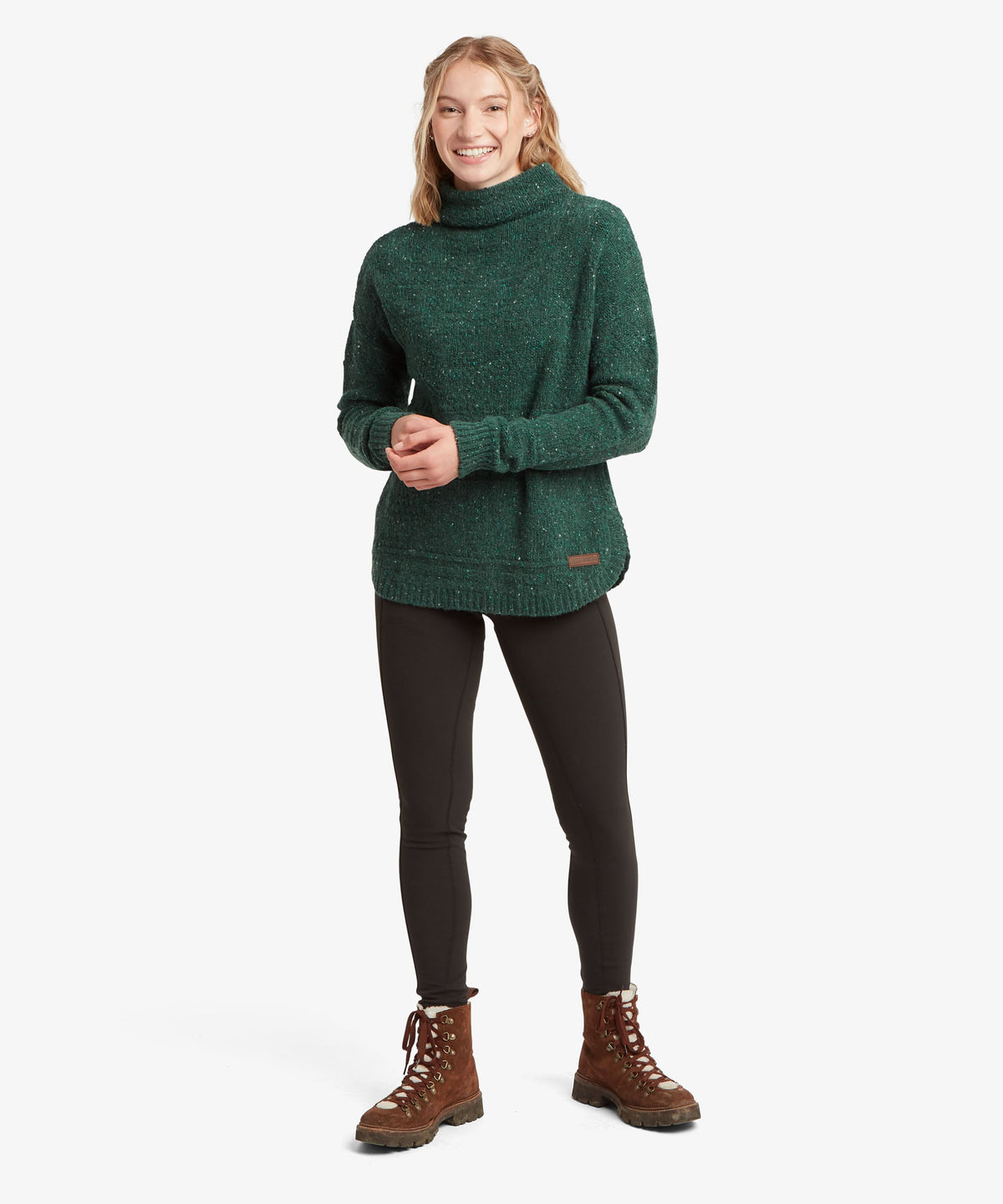 A female model wearing the green Yuden Sweater by Sherpa Adventure Gear with a high neckline.